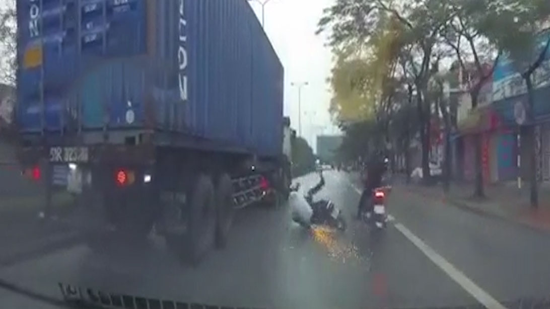 Hai thanh niên lái xe máy trượt chui vào gầm xe container